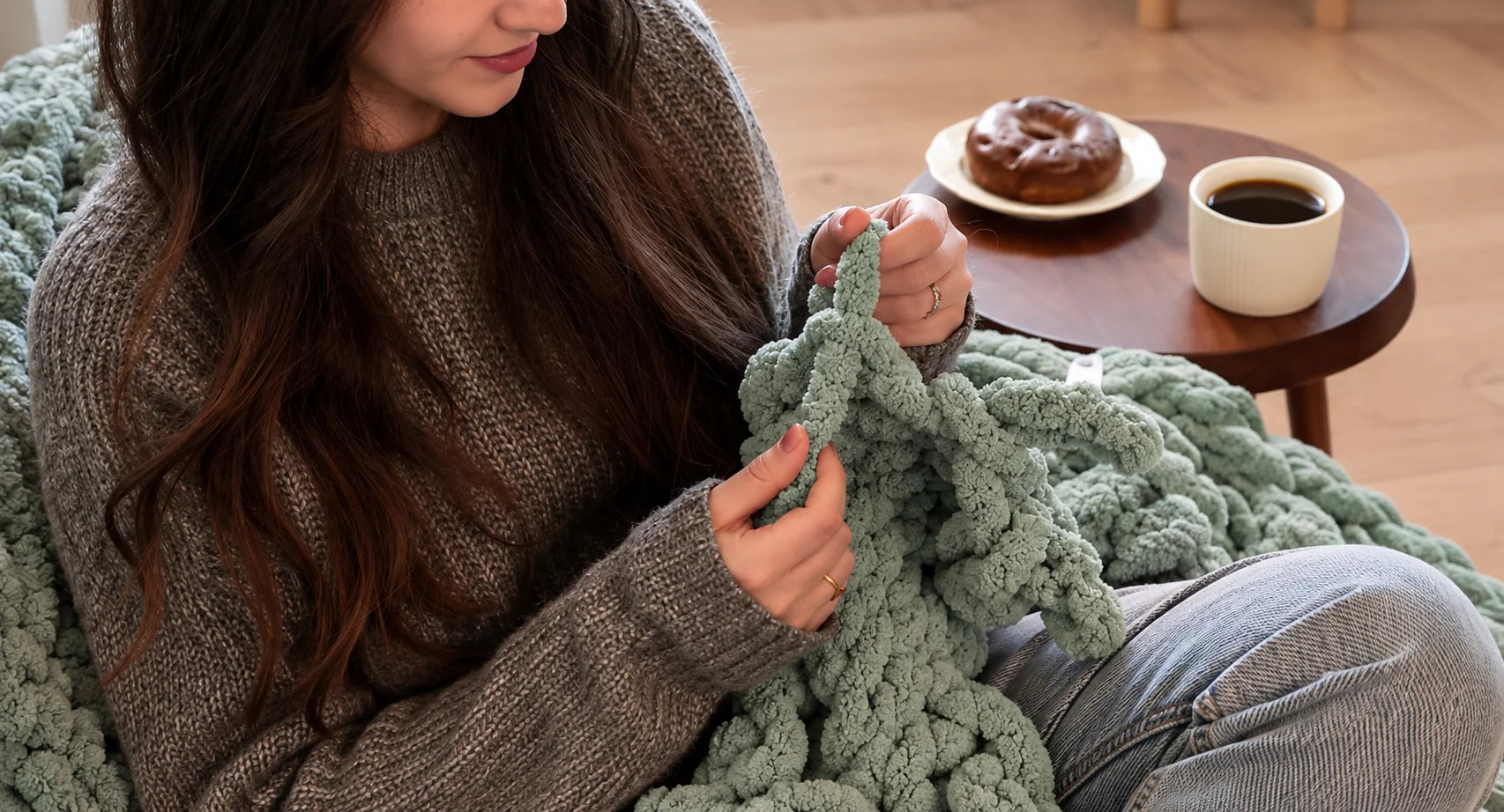 Hands working sage green chunky chenille yarn into a blanket